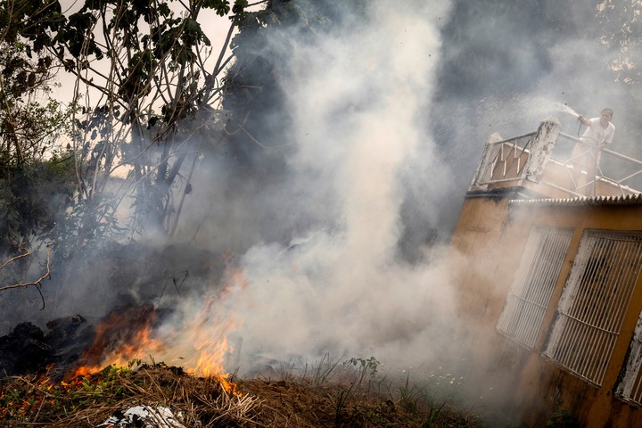 Una mujer intenta apagar este mes un incendio con una manguera en su casa a orillas del río Madeira en Porto Velho, en el estado de Rondonia (Brasil).